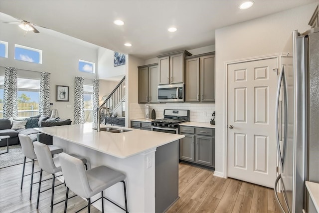 kitchen with light wood finished floors, gray cabinetry, appliances with stainless steel finishes, open floor plan, and a sink