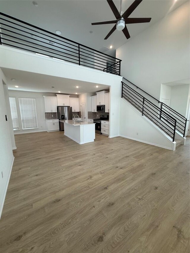 142 White Horses Dr, Kyle, TX 78640 - unfurnished living room featuring a ceiling fan, light wood-style flooring, stairs, a high ceiling, and recessed lighting