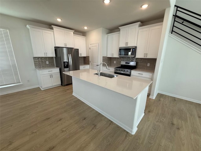 142 White Horses Dr, Kyle, TX 78640 - kitchen featuring appliances with stainless steel finishes, white cabinets, an island with sink, light wood finished floors, and tasteful backsplash