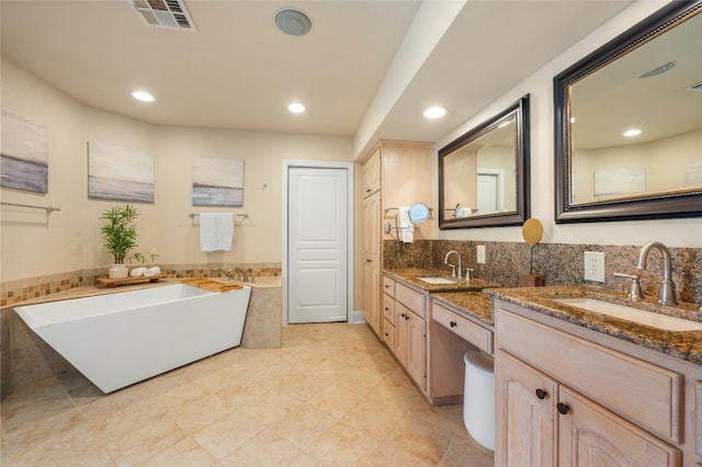 bathroom with double vanity, a freestanding bath, visible vents, and a sink