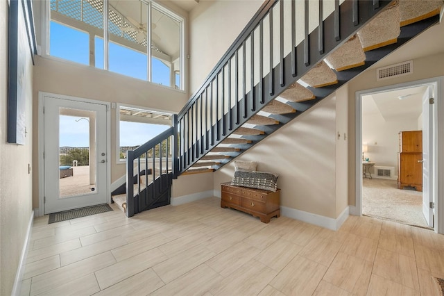 entrance foyer with baseboards, visible vents, a high ceiling, and stairs