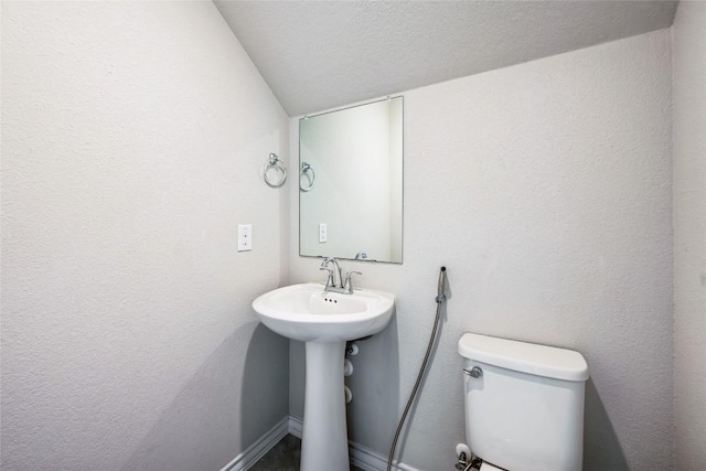 bathroom with baseboards, a textured wall, toilet, a textured ceiling, and a sink