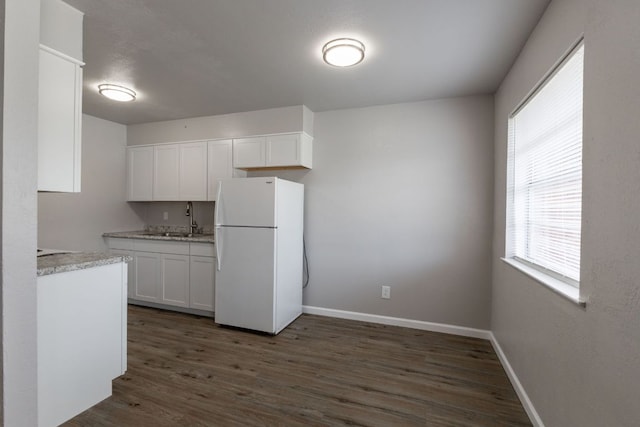 kitchen with baseboards, dark wood finished floors, freestanding refrigerator, white cabinetry, and a sink