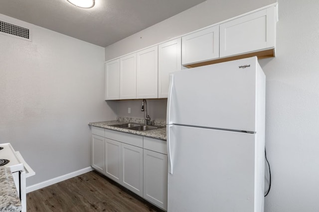 kitchen featuring white appliances, dark wood-type flooring, a sink, visible vents, and baseboards