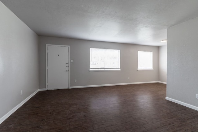 unfurnished room with a textured ceiling, dark wood-style flooring, and baseboards