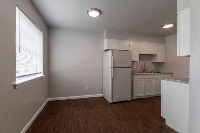 kitchen featuring dark wood-style flooring, freestanding refrigerator, white cabinetry, a sink, and baseboards