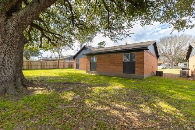 exterior space featuring a yard, brick siding, fence, and central air condition unit