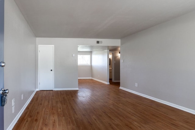 unfurnished room featuring dark wood-type flooring, visible vents, and baseboards