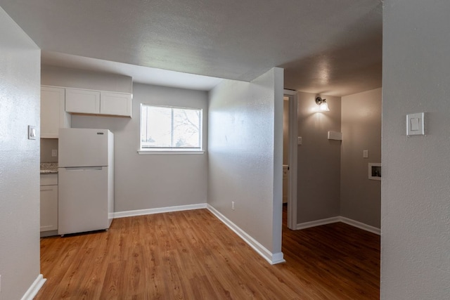 kitchen featuring light wood-type flooring, white cabinetry, baseboards, and freestanding refrigerator