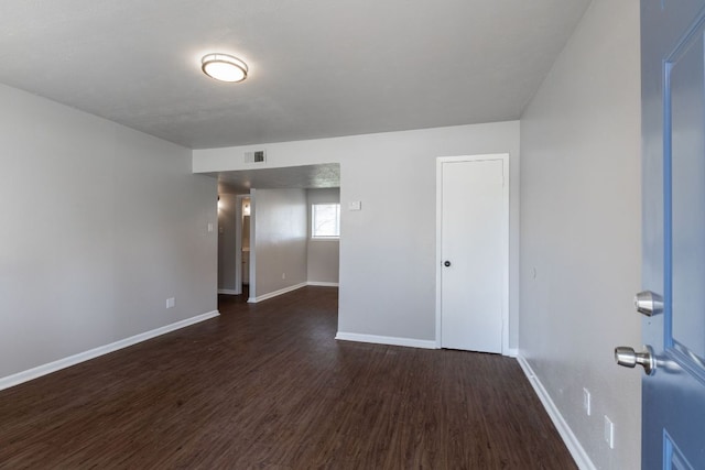 unfurnished room with visible vents, dark wood finished floors, and baseboards