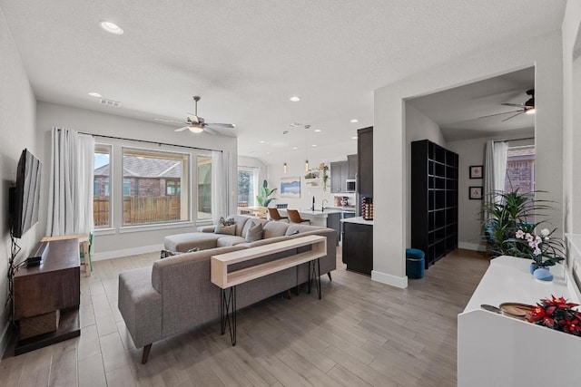 living area with a textured ceiling, light wood-type flooring, a ceiling fan, and recessed lighting