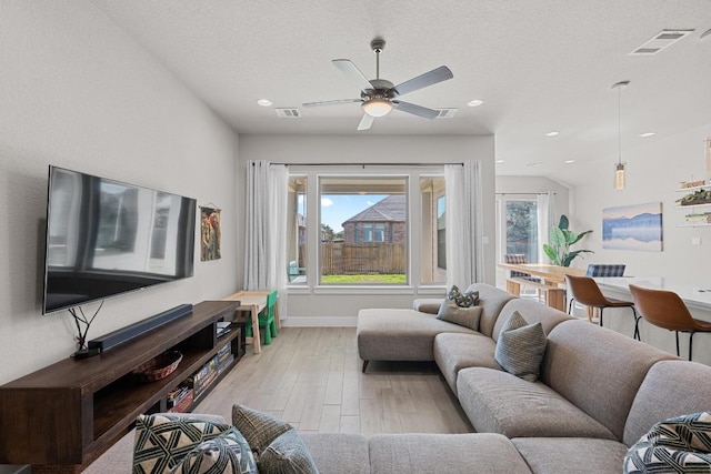 living room featuring a textured ceiling, light wood finished floors, plenty of natural light, and visible vents