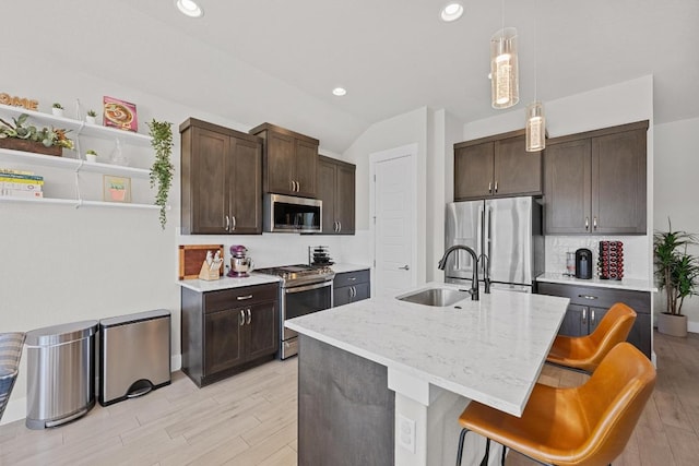 kitchen with stainless steel appliances, a sink, light wood-style floors, dark brown cabinets, and decorative light fixtures