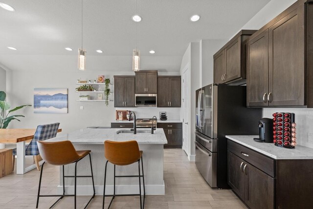 kitchen with dark brown cabinetry, appliances with stainless steel finishes, a breakfast bar, and a sink