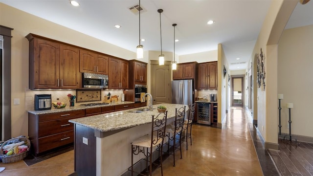 kitchen featuring beverage cooler, a sink, appliances with stainless steel finishes, backsplash, and a kitchen bar