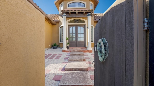 view of exterior entry with french doors, a tile roof, and stucco siding