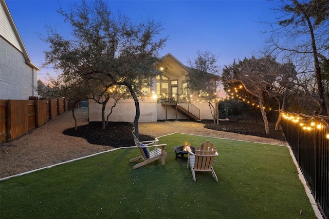 yard at dusk featuring an outdoor fire pit, a fenced backyard, and stairway