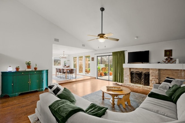 living area with ceiling fan with notable chandelier, visible vents, a stone fireplace, and wood finished floors