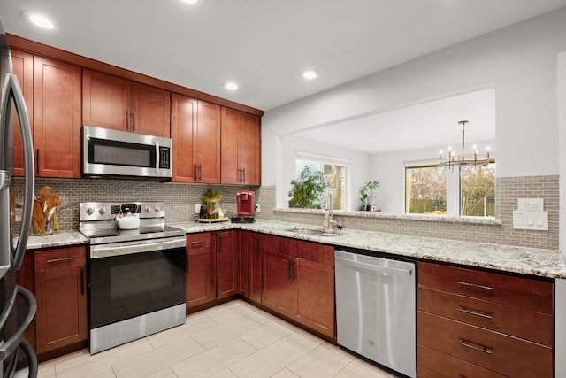 kitchen with a notable chandelier, a sink, stainless steel appliances, decorative backsplash, and light stone counters