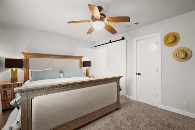 carpeted bedroom with a barn door, visible vents, baseboards, and ceiling fan
