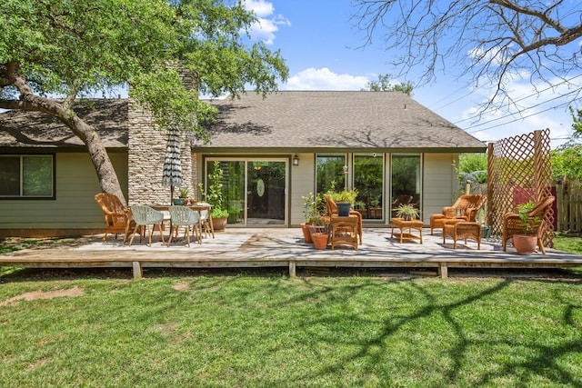 rear view of house with fence, a deck, a lawn, and roof with shingles