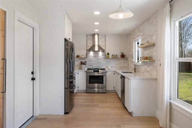 kitchen featuring stainless steel appliances, a sink, light countertops, wall chimney range hood, and open shelves