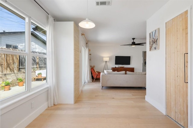 corridor featuring light wood-style floors, a wealth of natural light, visible vents, and baseboards