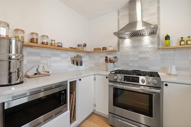 kitchen featuring open shelves, stainless steel appliances, tasteful backsplash, light countertops, and wall chimney range hood