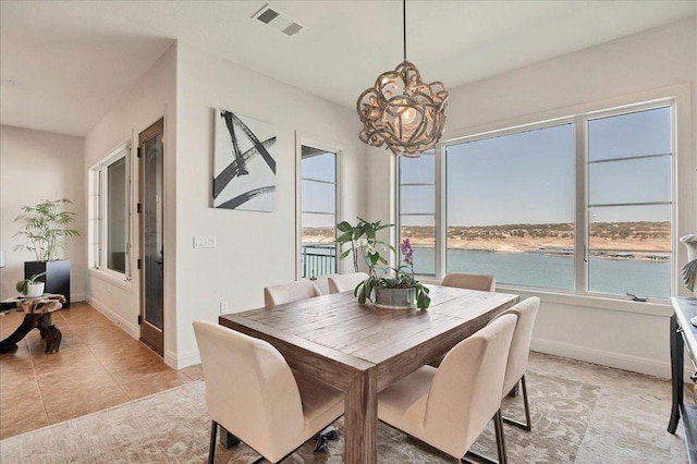 dining area with light tile patterned floors, baseboards, visible vents, a water view, and a chandelier