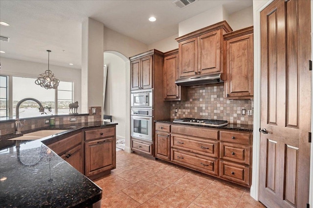 kitchen featuring visible vents, appliances with stainless steel finishes, brown cabinetry, a sink, and under cabinet range hood