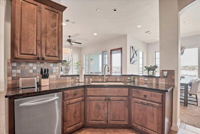 kitchen with a sink, visible vents, stainless steel dishwasher, backsplash, and dark stone counters