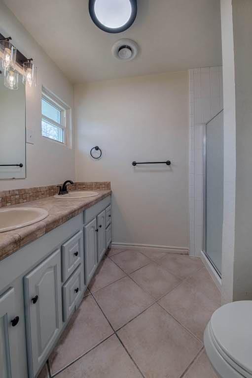 full bath with double vanity, a sink, a shower with shower door, and tile patterned floors