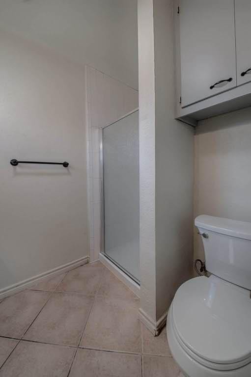 bathroom with a stall shower, baseboards, toilet, and tile patterned floors