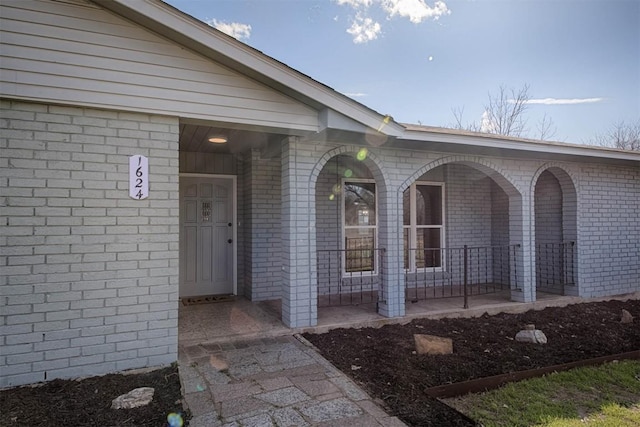 doorway to property with a porch and brick siding