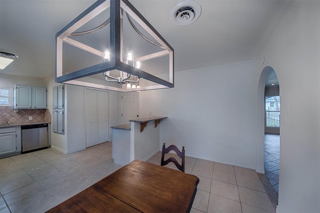 kitchen with arched walkways, decorative backsplash, dishwasher, a chandelier, and light tile patterned flooring