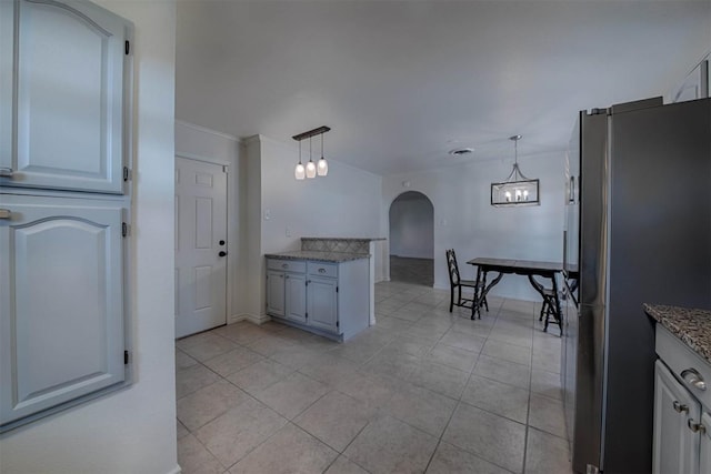 kitchen featuring freestanding refrigerator, hanging light fixtures, arched walkways, and light tile patterned floors