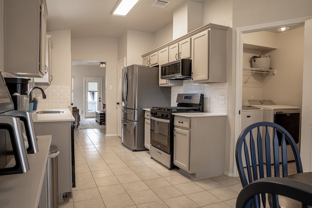 kitchen with light tile patterned floors, a sink, light countertops, appliances with stainless steel finishes, and washer and clothes dryer