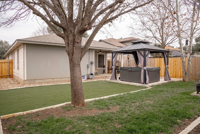 rear view of property featuring a hot tub, a fenced backyard, a gazebo, a yard, and a patio area