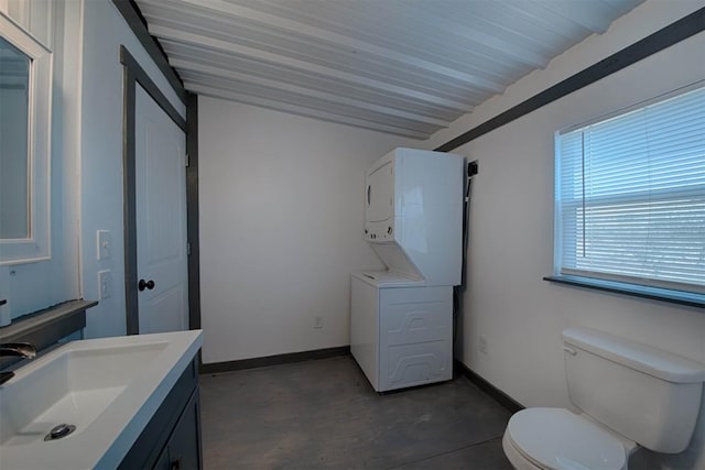 bathroom with stacked washer / drying machine, toilet, vanity, concrete floors, and baseboards