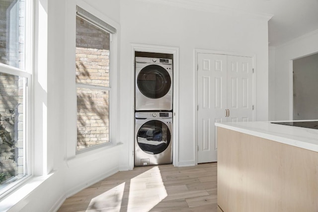 washroom featuring crown molding, laundry area, stacked washing maching and dryer, and a healthy amount of sunlight