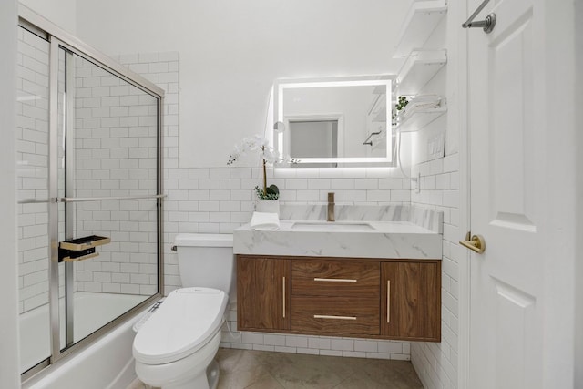 bathroom with bath / shower combo with glass door, vanity, toilet, and tile walls