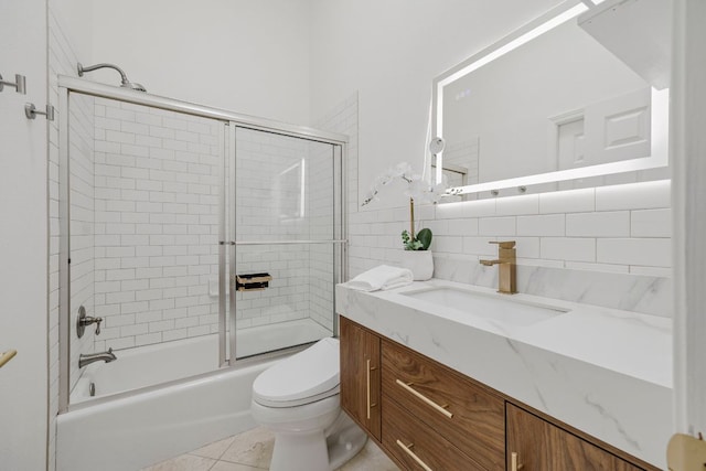 full bathroom featuring toilet, shower / bath combination with glass door, tile patterned floors, vanity, and tile walls