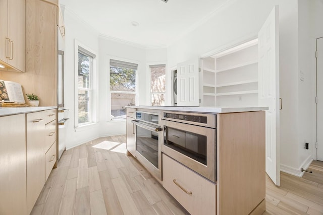 kitchen featuring light wood-style floors, stainless steel oven, light countertops, and ornamental molding