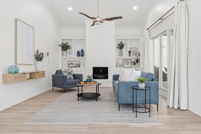 living area with a fireplace, wood finished floors, a ceiling fan, baseboards, and ornamental molding