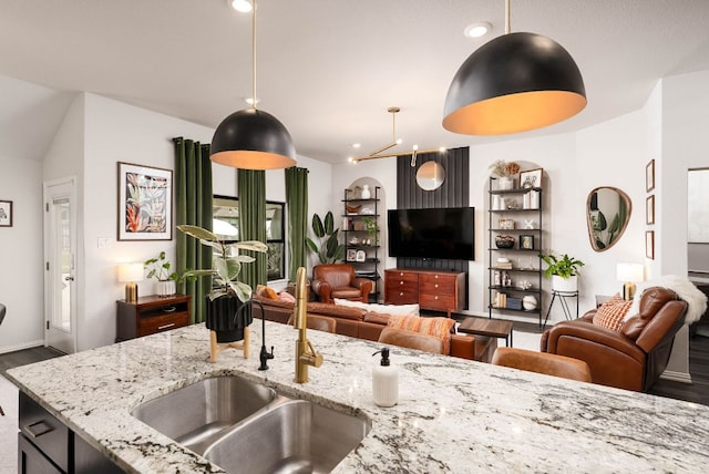 kitchen with light stone counters, decorative light fixtures, open floor plan, a sink, and wood finished floors