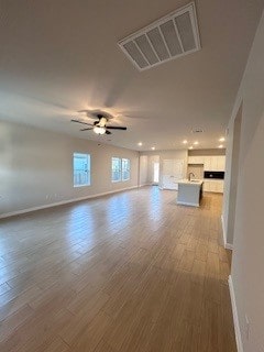 unfurnished living room featuring a ceiling fan, wood finished floors, visible vents, and baseboards