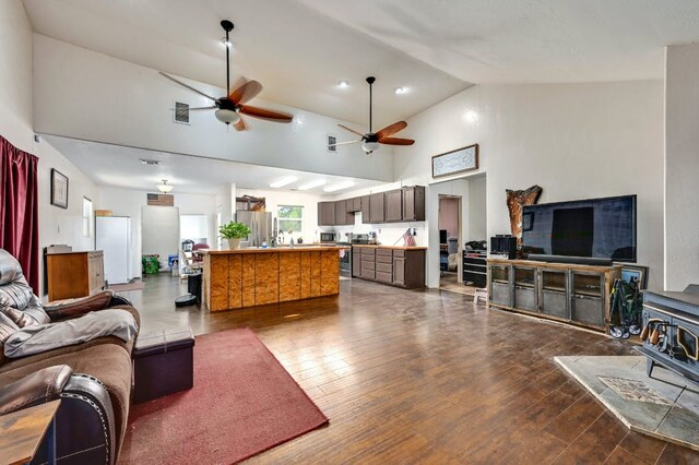 living room with visible vents, dark wood-style floors, ceiling fan, a wood stove, and high vaulted ceiling