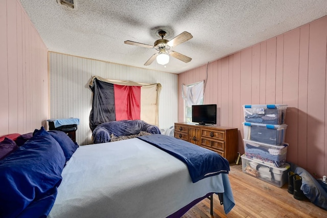 bedroom featuring ceiling fan, a textured ceiling, visible vents, and wood finished floors