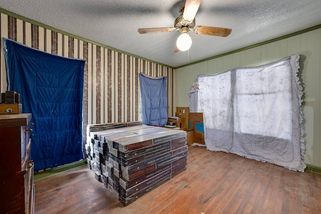 bedroom with wallpapered walls, a textured ceiling, and wood finished floors