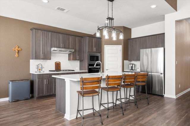 kitchen featuring under cabinet range hood, a sink, visible vents, light countertops, and appliances with stainless steel finishes